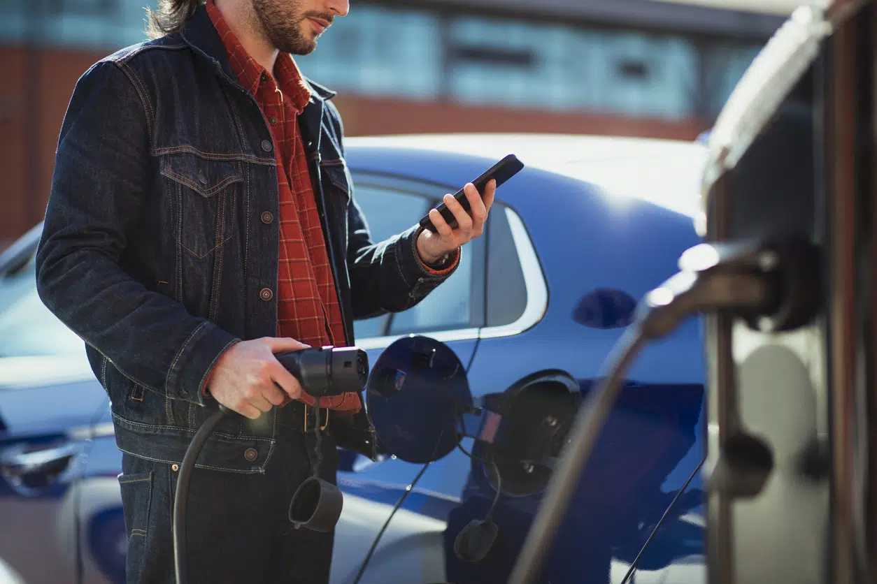 Man plugging in an electric car charger while holding phone to pay image