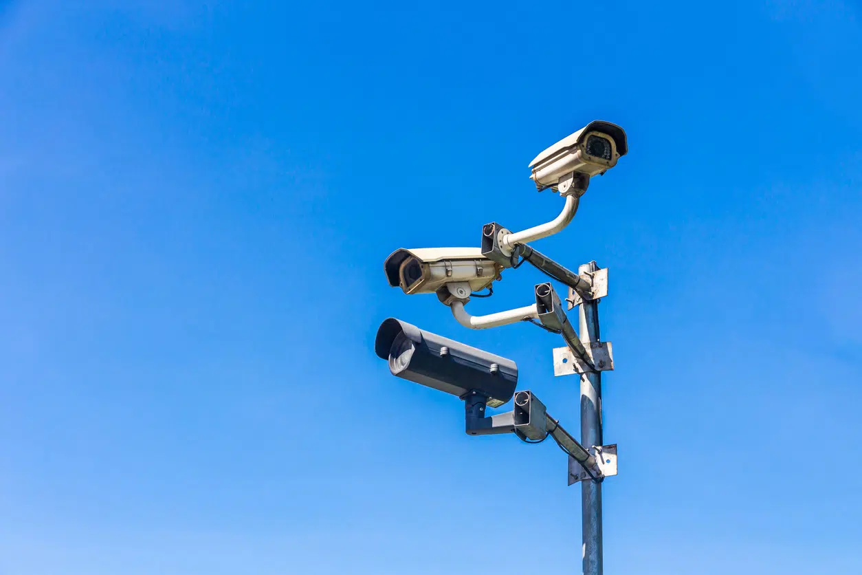 Old security camera CCTV sits on a pole with blue sky image
